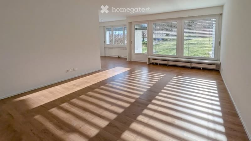 Empty room with wooden flooring, large windows, and white walls. No furniture or equipment present.