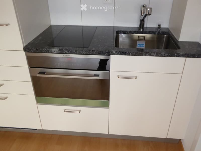 Modern kitchen with white cabinets, granite countertop, stainless steel sink, and built-in oven.