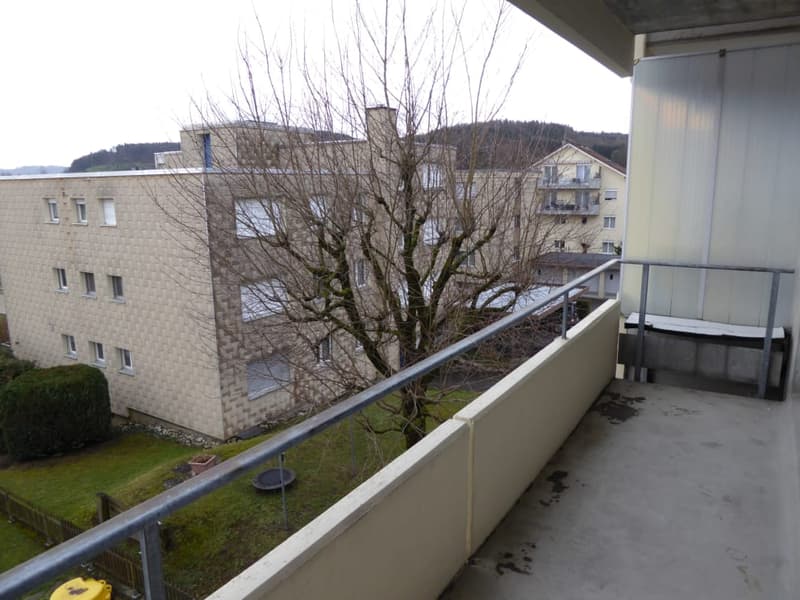 Balcony with metal railing, overlooking a residential area with buildings and a tree.