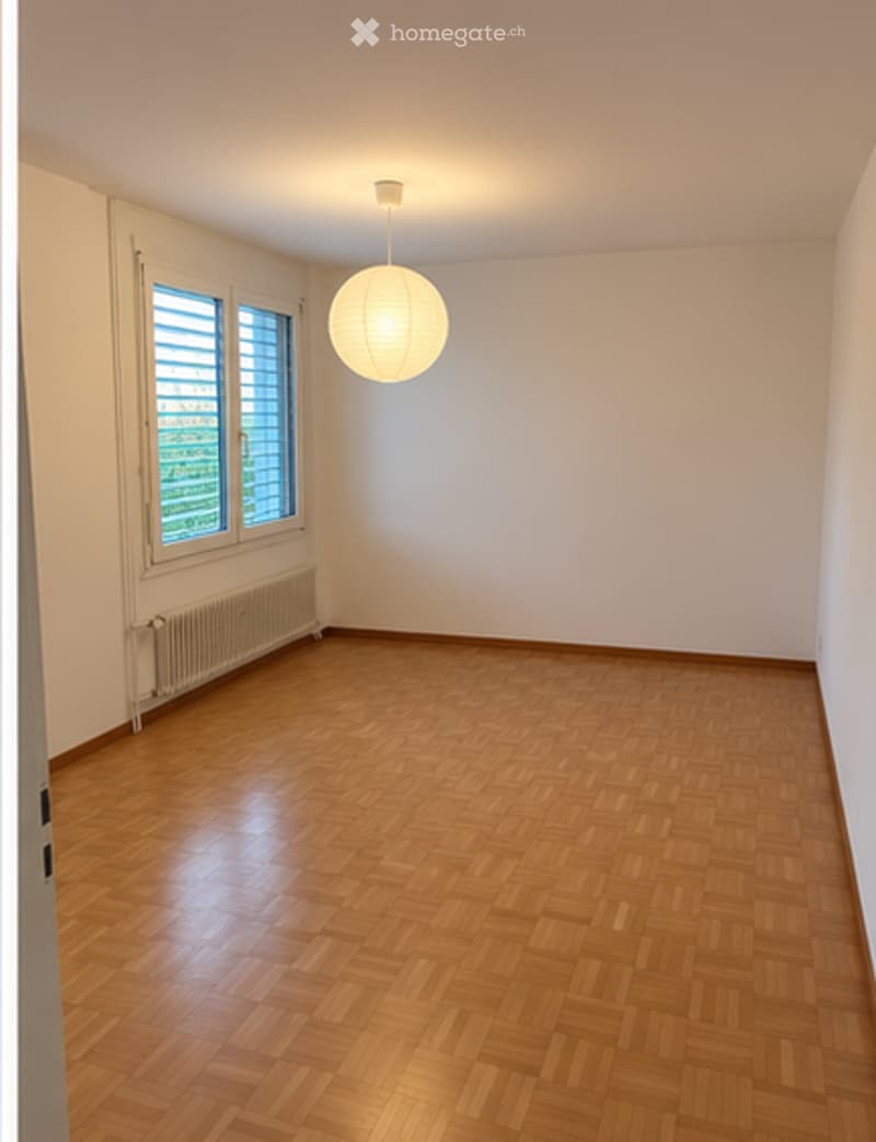 Empty room with wooden flooring, white walls, large window with blinds, and a hanging light fixture.