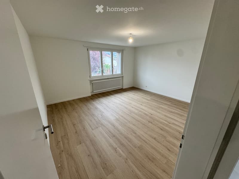 Empty room with wooden flooring, white walls, and a window with a radiator below it. The room has a slanted ceiling typical of an attic space.
