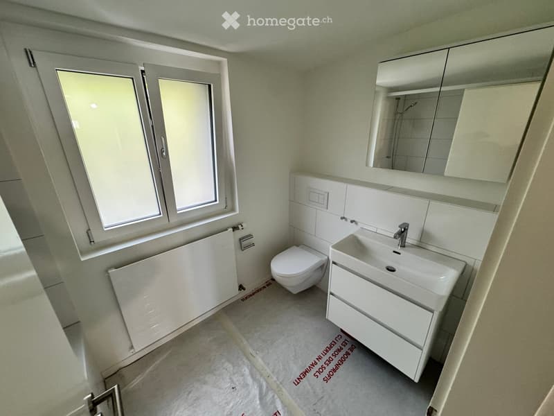 Modern bathroom with white tiles, a toilet, a sink with a faucet, a mirror, and built-in cabinets. The room features large windows with frosted glass and a radiator.