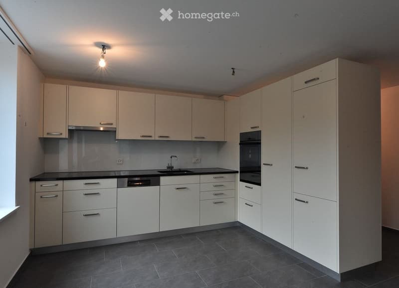 Modern kitchen with light-colored cabinets, stainless steel appliances, and dark tiled flooring.