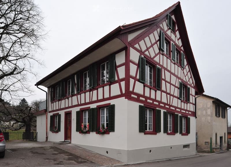 Two-story traditional half-timbered house with red and white exterior, green shutters, and flower boxes on the windows.