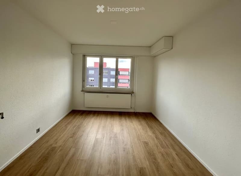 Empty room with wooden flooring, white walls, and a large window with a radiator below it. No furniture or equipment is present.