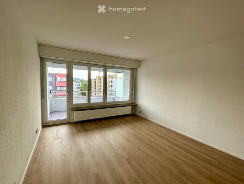 Empty room with wooden flooring, large windows, and access to a balcony.