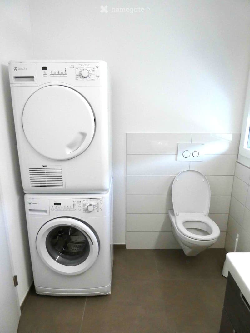 Bathroom with a washing machine and dryer stacked vertically, a toilet, and a small window.
