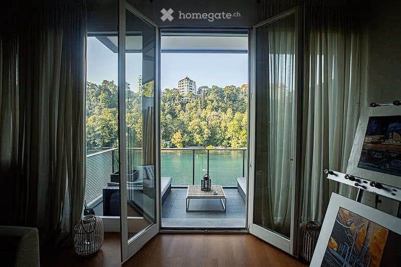 Modern living room with large glass doors opening to a balcony, featuring a sofa, small table, and decorative items.