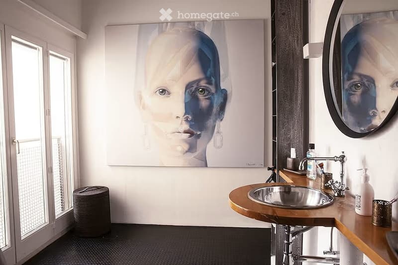 Modern bathroom with a large round mirror, wooden sink, and a large abstract portrait on the wall.