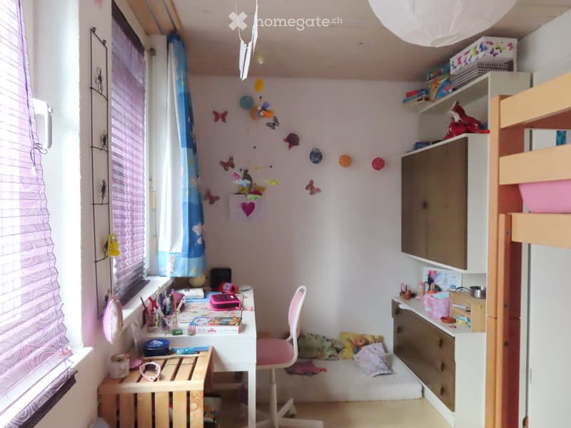 Cozy children's bedroom with a bunk bed, desk, chair, and various toys and decorations.