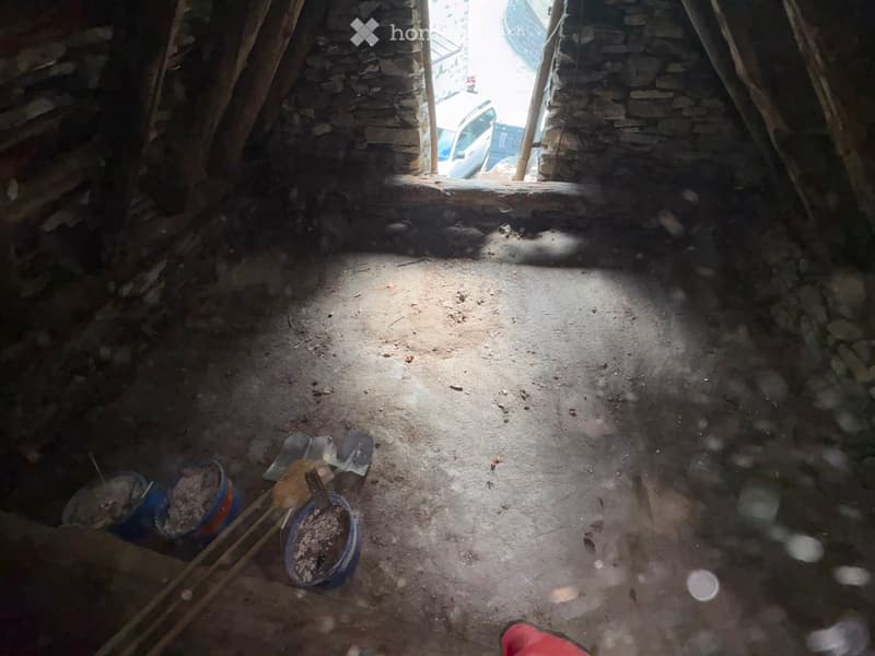 Empty room with stone walls and wooden beams, concrete floor, and scattered construction materials including buckets and tools.