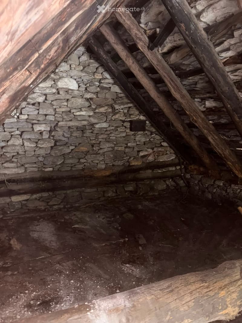 Empty attic space with exposed wooden beams and stone walls, showing unfinished construction and natural lighting from the roof opening.