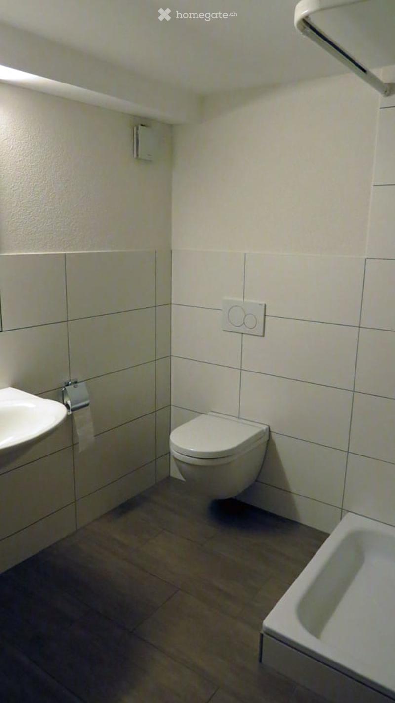 Bathroom with a white sink, a white toilet, a mirror, white tiles on the walls and wooden floor