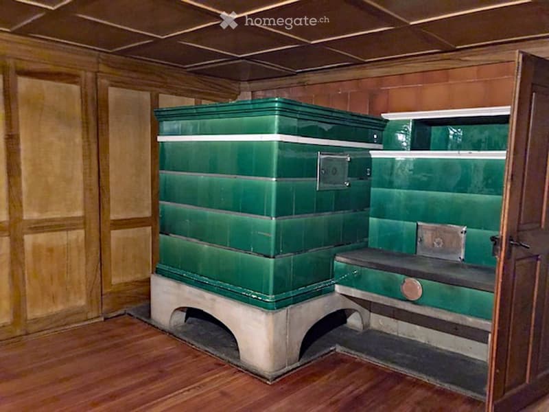 interior of room, wooden wall panels, green tiled furnace with wooden bench, wooden floor