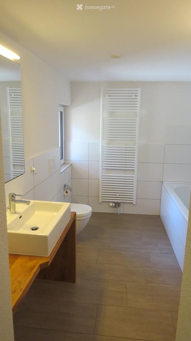 Bathroom: white sink, wooden countertop, white bathtub, white tiles, toilet, mirror, white towel rack