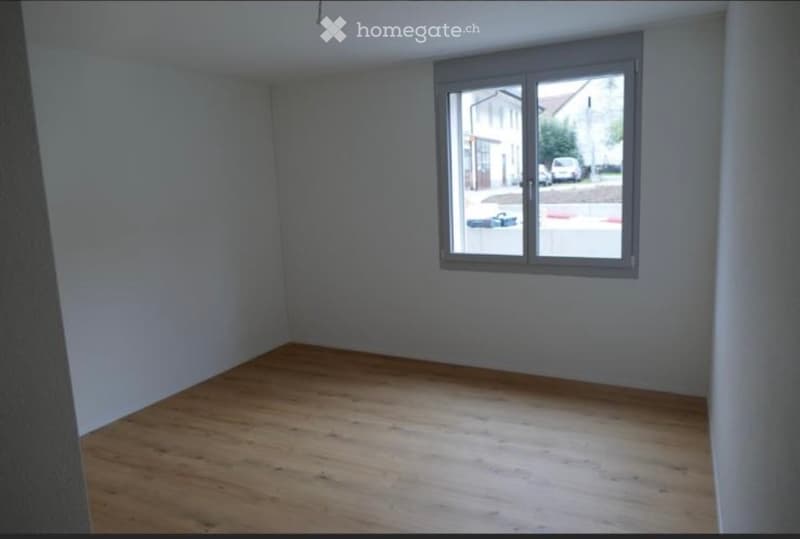 Empty room with wooden flooring and a large window showing a street view.