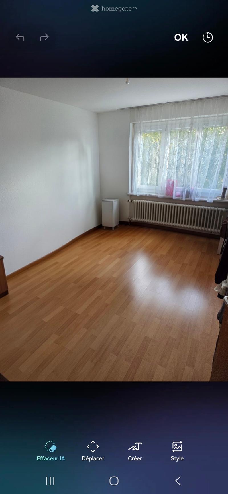 Empty room with wooden flooring, white walls, and a window with sheer curtains. A small white cabinet is visible near the window, and a radiator is below the window.