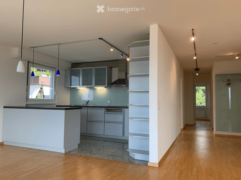 Modern kitchen with light grey cabinets, a central island, and built-in appliances. The space features wooden flooring, pendant lights, and a sleek design with open shelving.