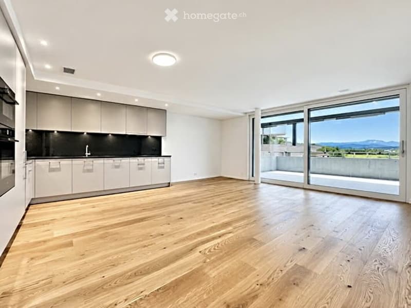 Bright, open-plan space with light wooden flooring, modern white kitchen units, and large floor-to-ceiling windows offering a scenic view.