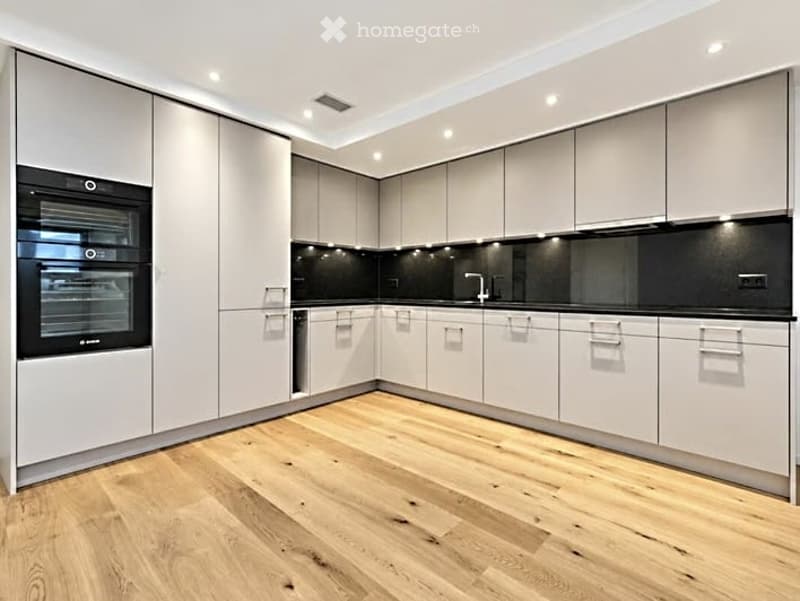 Modern kitchen with light grey cabinets, wooden flooring, and built-in oven.