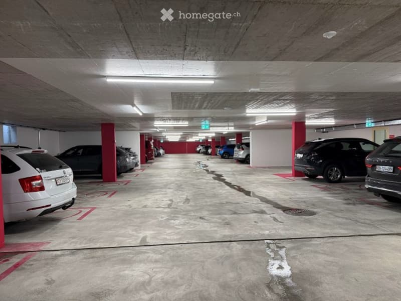 Underground parking lot with several parked cars, concrete pillars, and marked parking spaces.