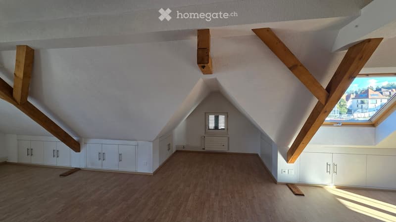 Empty attic room with wooden beams, white cabinets, wooden flooring, and skylight windows.