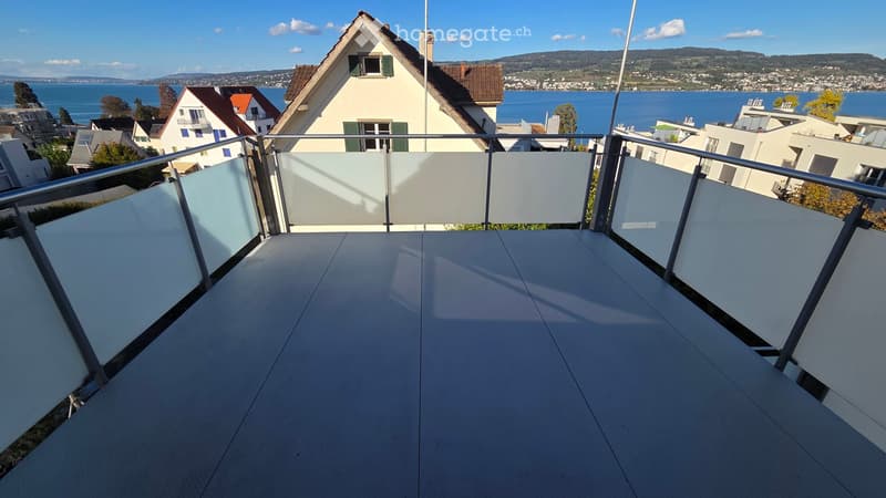 Balcony with modern glass balustrade, overlooking a scenic lake and town view.