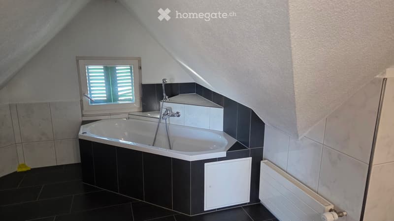 Modern bathroom with a bathtub, sleek black and white tiles, a window with blinds, and a radiator.