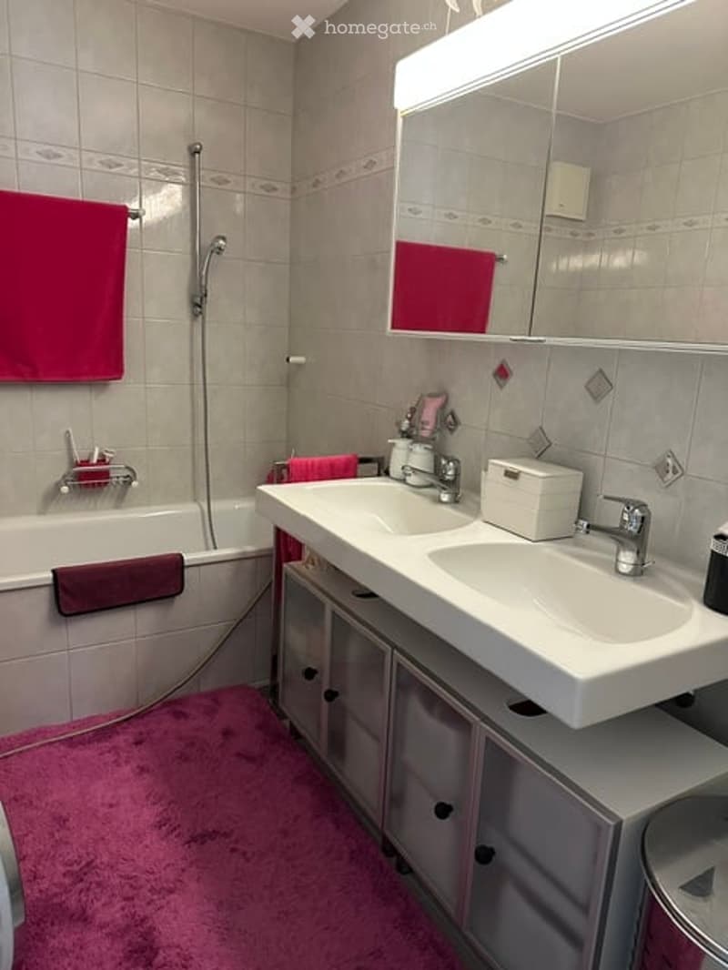 Modern bathroom with a white bathtub, double sink, large mirror, and pink towels.