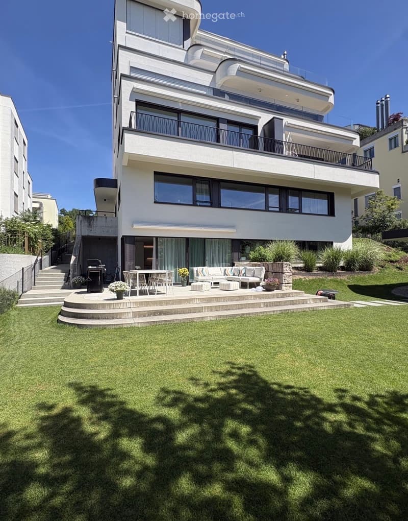 Modern house with a spacious garden and outdoor seating area featuring a sofa, ottomans, a table, and chairs.