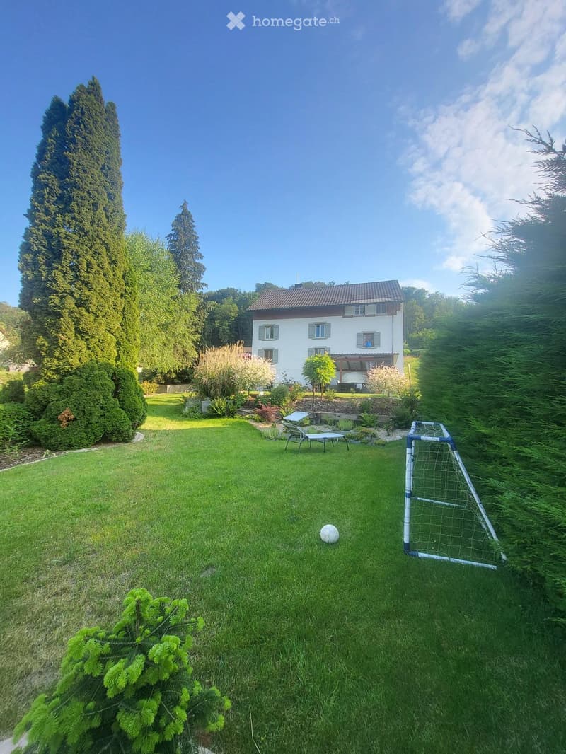A well-maintained garden with a lawn, a small soccer goal, a soccer ball, and a lounge chair near the house.
