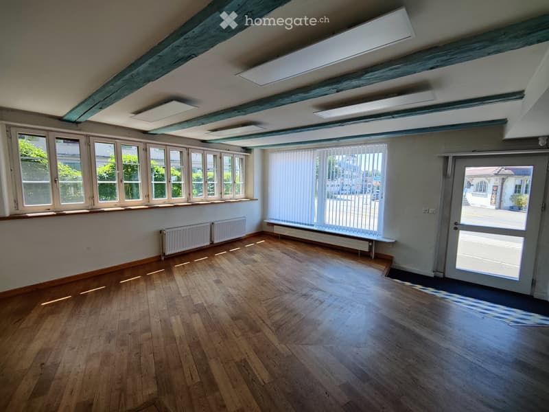 Empty room with wooden flooring, large windows, radiators, and exposed wooden beams on the ceiling.