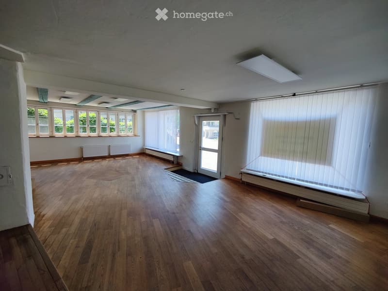 Empty room with wooden flooring, large windows with blinds, radiators, and a door leading outside.