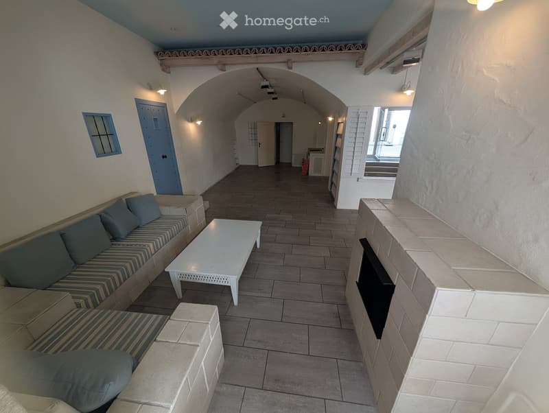 A furnished room with a sofa, coffee table, and a fireplace, featuring tiled flooring and arched doorways.