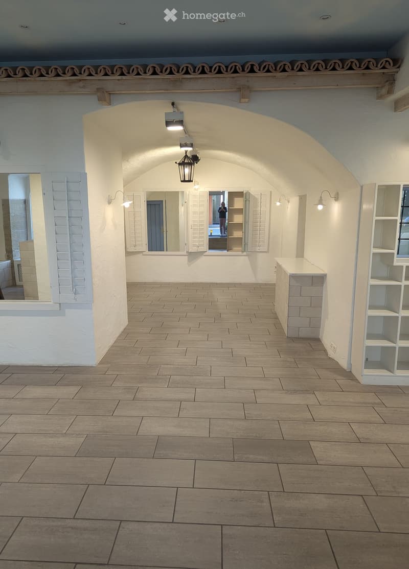 empty, wooden beams, arched opening, wood tile flooring, white walls, mounted lights, open door with mirrors and shelves, cabinet, outlet