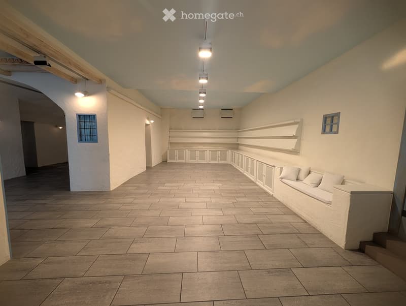 Empty room with tiled floor, white walls, built-in bench seating, and built-in cabinets. Exposed wooden beams on the ceiling and recessed lighting.