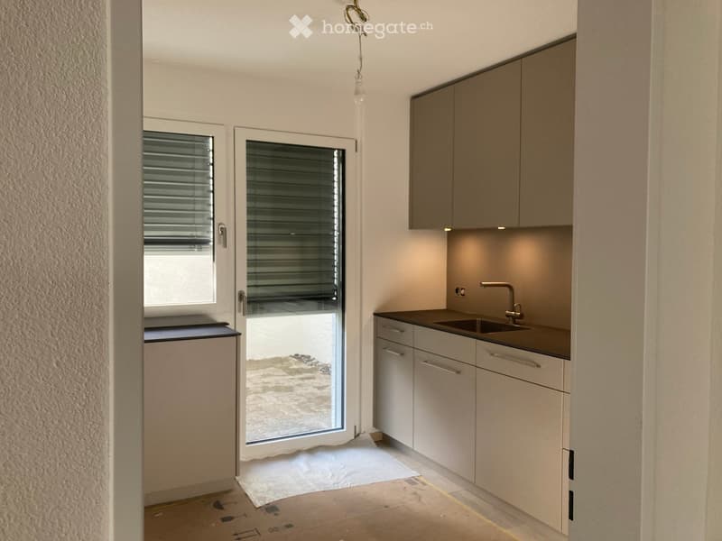 Modern kitchen with white cabinets, a sink, and a faucet. The space features a large window with blinds and a door leading outside.