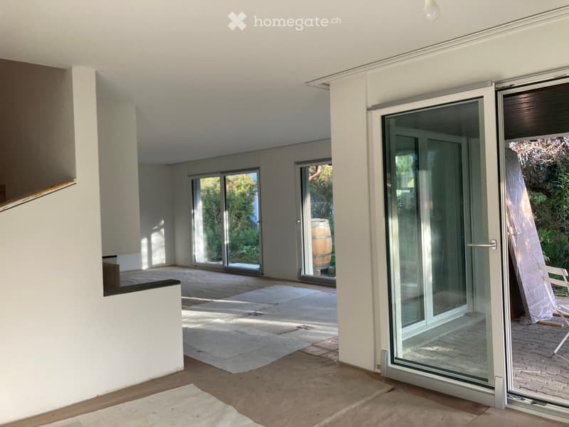 An unfurnished room with large glass sliding doors leading to an outdoor area, featuring a wooden barrel and a white plastic chair in the background.