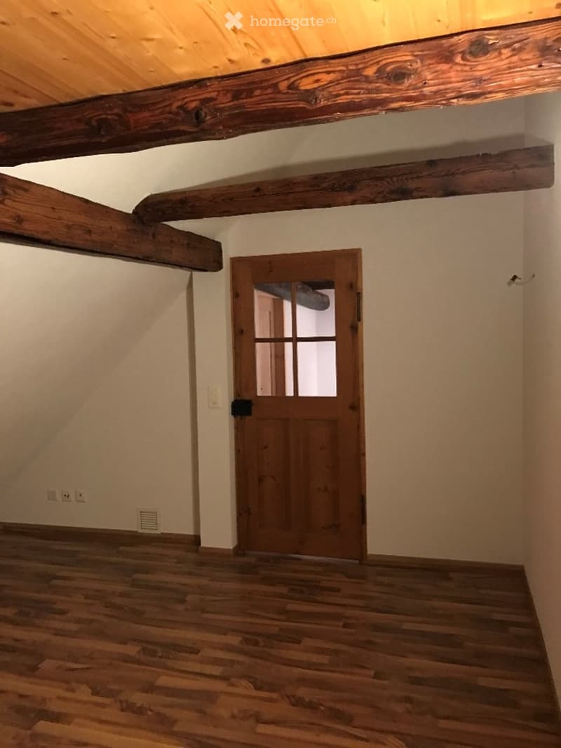 Empty room with exposed wooden beams, wooden floor, and a wooden door with glass panels.