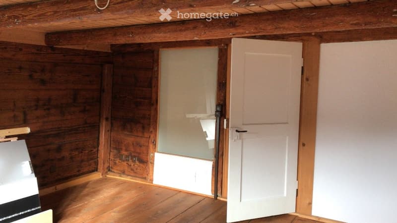 Empty room with wooden walls and floor, featuring a partially open door leading to another room.