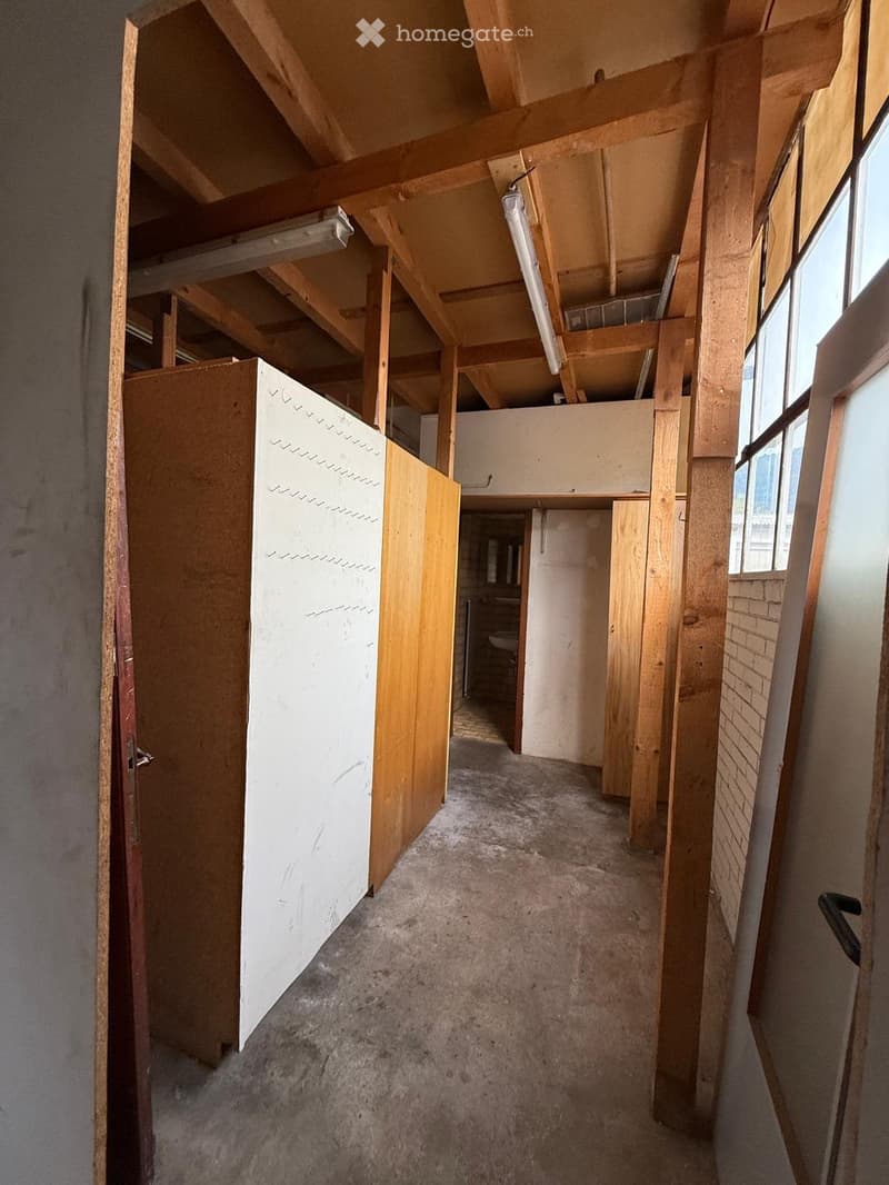 Empty hallway with exposed wooden beams, unfinished walls, and carpeted floor. A partially open door leads to a room with a visible toilet.