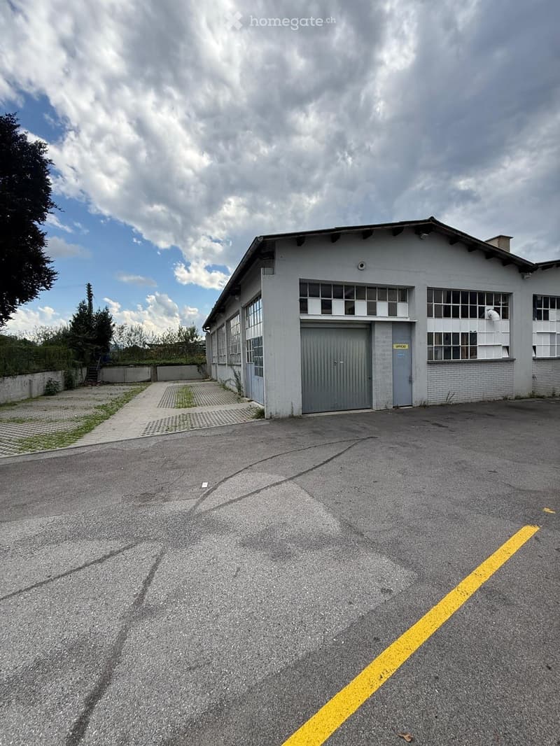 A single-story industrial building with a large garage door, multiple windows, and a paved parking area.