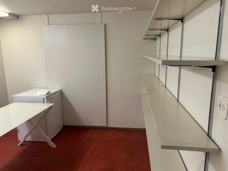 Empty room with white walls, red floor, shelves, and a pegboard wall.