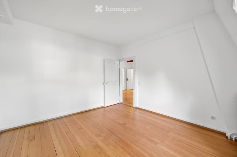 Empty room with white walls and wooden flooring, featuring a single door leading to another room.