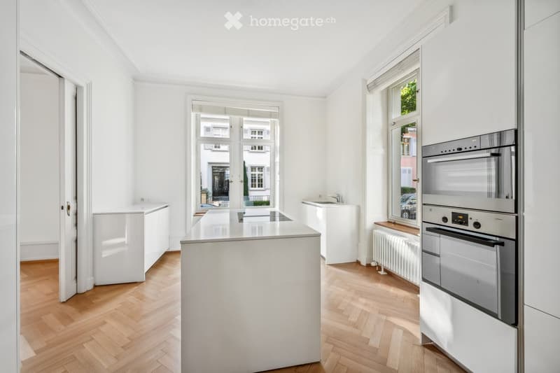 Modern, minimalist kitchen with white cabinetry, a central island, and integrated appliances including an oven and sink.