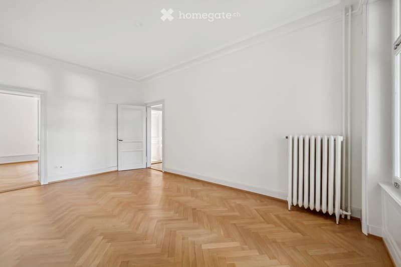 Empty room with white walls, wooden herringbone flooring, and a white radiator on one wall. No furniture or equipment present.