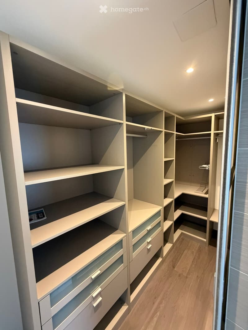 Spacious, well-lit walk-in closet with built-in shelves and drawers, featuring a wooden floor and modern design.