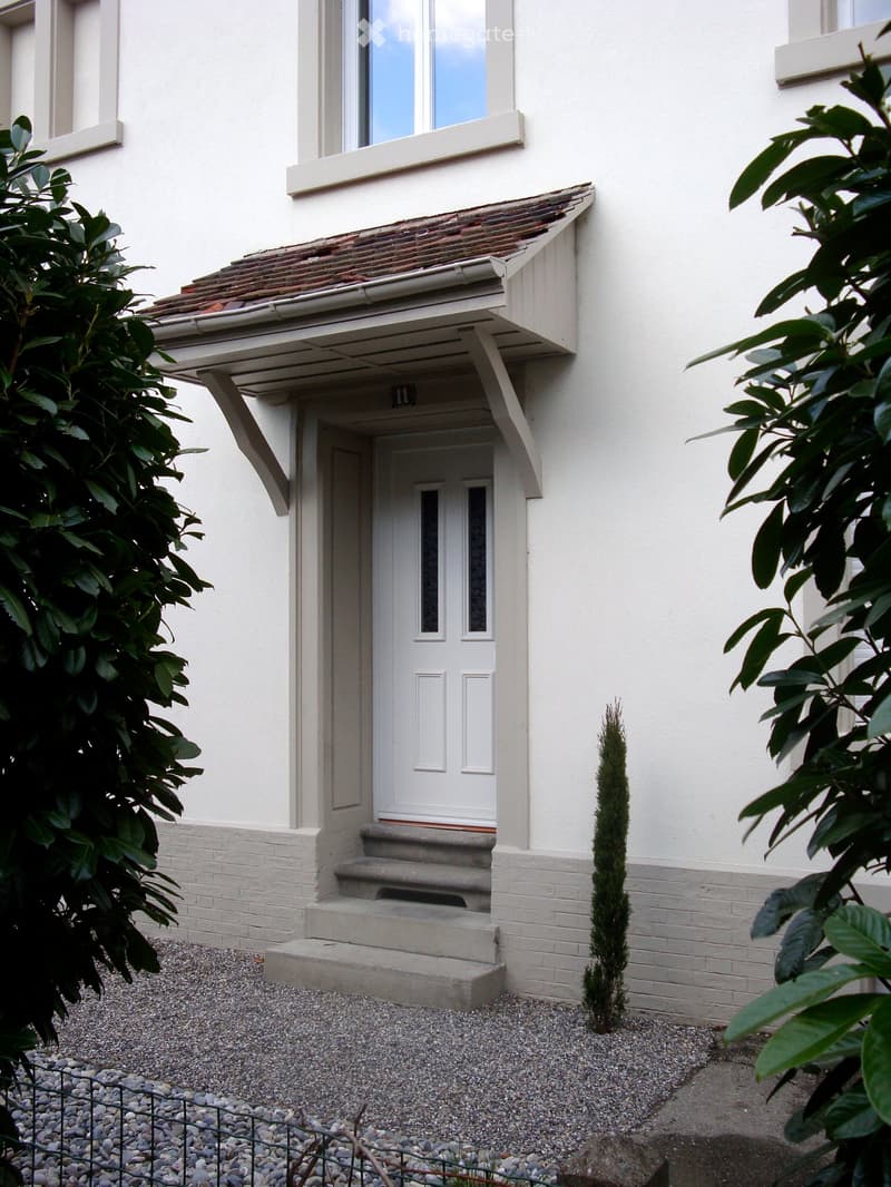 Two-story house with white exterior, tiled roof, and a small porch with steps leading to the front door.