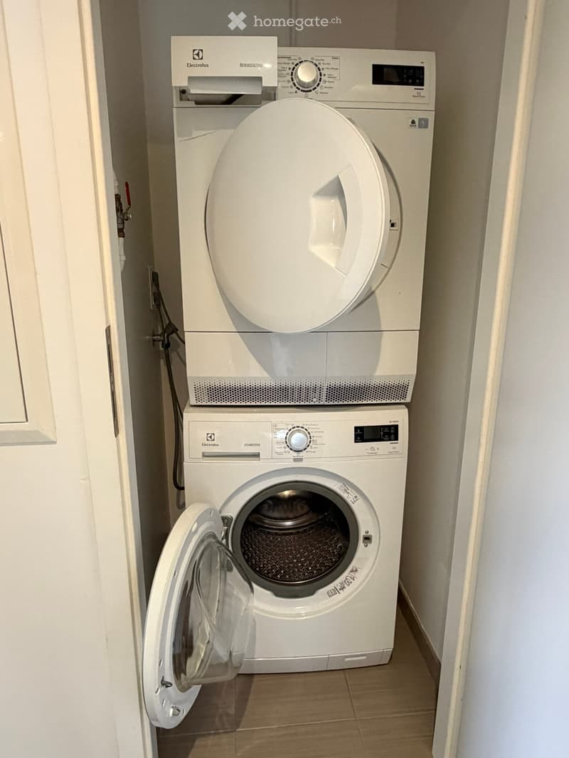 A compact bathroom with a white washing machine and dryer stacked vertically, both with control panels and dials.