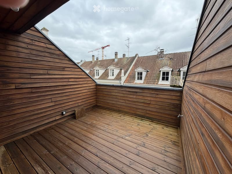 Wooden balcony with wooden decking, wooden walls, and a view of neighboring rooftops.